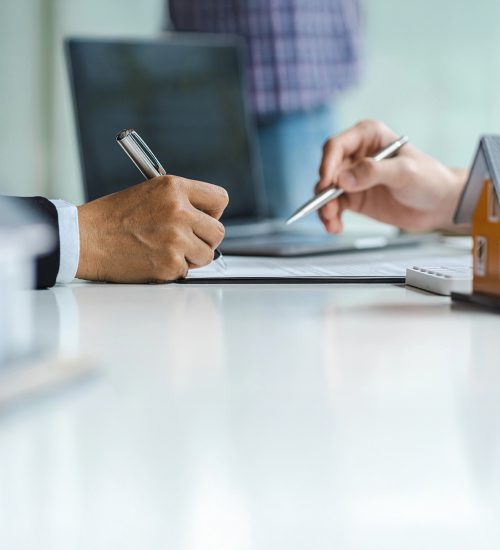 Real estate agent with house model hand putting signing contract, hands holding pen to sign a contract close up.
